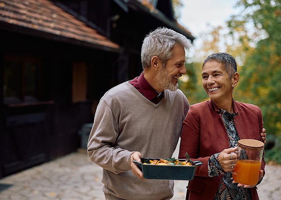 A happy mature couple talking while bringing food and drinks out to the patio. — Drazen Zigic // Shutterstock