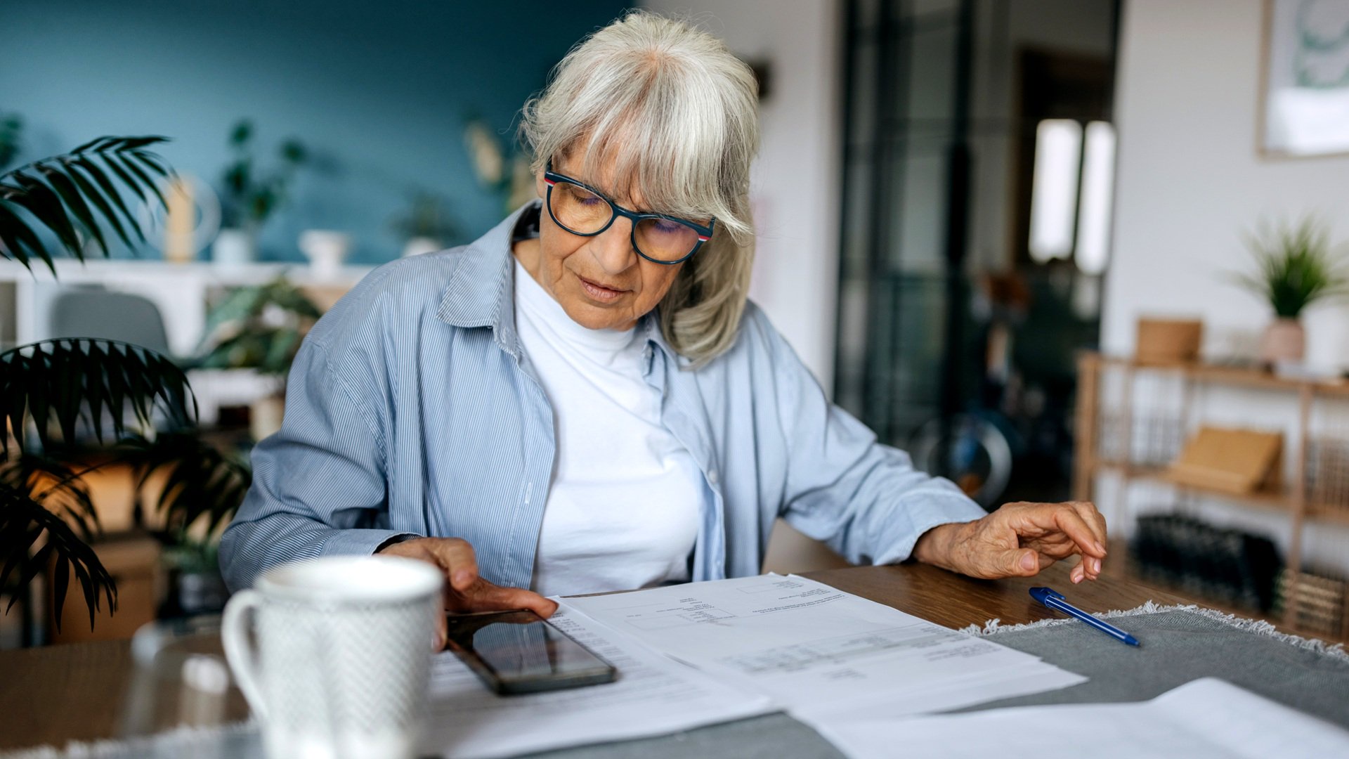 Discover a mature senior woman sits at table in home reviewing bills while budgeting with calculator