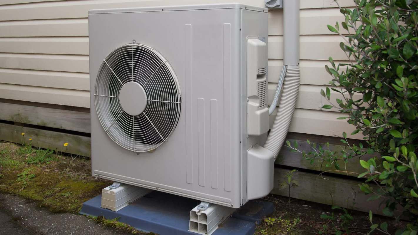 An outdoor air conditioning unit located beside a building, surrounded by small plants.