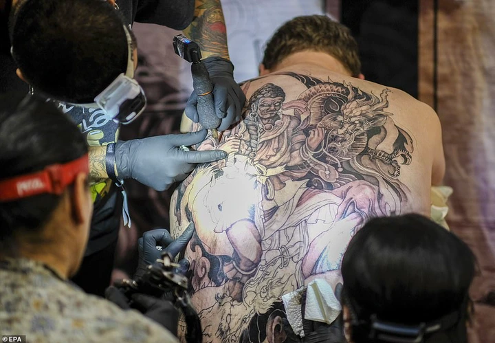 The convention encourages people to show their 'real selves' by adding tattoos to their body. Pictured: Three tattoo artists all working simultaneously on a man's partially complete, fully-back tattoo