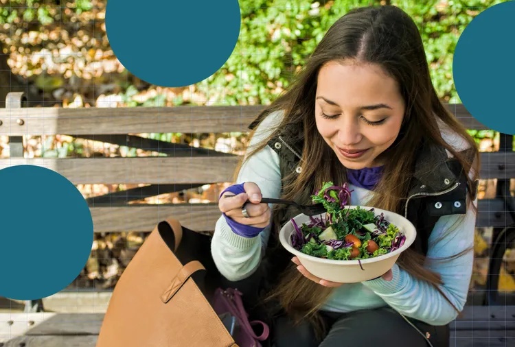 A person sitting outdoors on a bench eating a bowl of salad