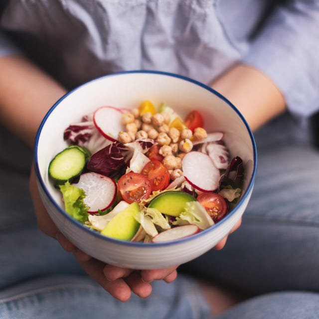 Green vegan breakfast meal in bowl with spinach, arugula, avocado, seeds and sprouts. Girl in leggins holding plate with hands visible, top view. Clean eating, dieting, vegan food concept